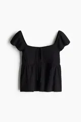 Top corto negro en punto arrugado con escote corazón, manga circular y sección cut-out con cordón para ajustar en el busto. Modelo ajustado sobre el busto con copas preformadas fruncidas y peplum con leve vuelo.