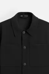 Sobrecamisa negra de corte cuadrado con cuello solapa, manga larga con puños abotonados, bolsillos de parche en el pecho, bolsillos laterales y cierre frontal con botones.