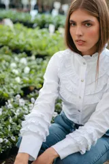 Camisa blanca de algodón con broderie, cuello alto con volados y mangas largas con puños abotonados y volados.