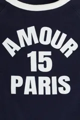 Remera corta azul marino con mangas raglán blancas. Estampado frontal con la palabra "Amour", el número "15" y la palabra "Paris" en blanco.