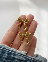 Caravanas de acero dorado con diseño de moño, elegantes y brillantes.
