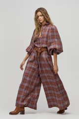 Camisa larga de lino a cuadros color avellana, con cuello camisero clásico, mangas largas abullonadas con puños elásticos, botones de nácar frontales y ruedo curvo, un poco más largo atrás. Incluye cinturón de cuero marrón.