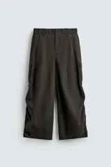 Pantalón cargo de corte ancho y relajado, color verde oscuro o negro, con cintura elástica, bolsillos laterales de parche y bolsillos traseros de vivo. Presenta pliegues verticales marcados en la parte delantera y cordones ajustables en los bajos.