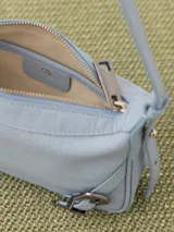 Mini cartera bandolera color celeste con textura granulada, correa fina al tono y detalles de hebillas metálicas plateadas.