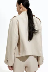 Chaqueta corta color beige, de corte oversized, con cuello clásico, charreteras abotonadas, bolsillos laterales y trabilla con botón en los puños.