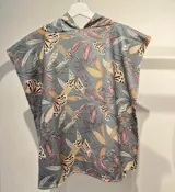 Poncho toalla con capucha, estampado con diseño de hojas y mariposas en tonos rosa, naranja y gris sobre fondo celeste.