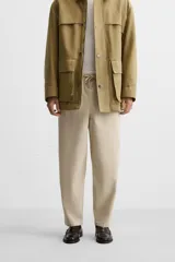 Pantalón de hombre color beige, corte carrot fit, con cintura elástica ajustable con cordón, bolsillos frontales y bolsillo trasero de plastrón.
