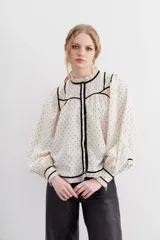 Camisa cruda de algodón con calce relajado y cuello redondo. Detalles de velvet negro y broderie en escote, puños y ruedo.