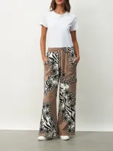 Pantalón de tela color marrón con estampado de flores blancas y negras, de corte palazzo con bolsillos laterales y cintura con cordón.