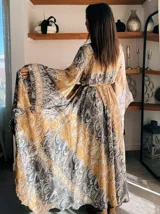 Kimono largo de seda con estampado floral en tonos verde, marrón y beige. Tiene mangas amplias y corte cruzado con lazo ajustable en la cintura.