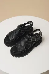 Sandalias negras de cuero con plataforma y tiras entrecruzadas con costuras blancas.