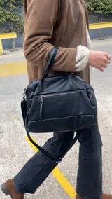 Cartera negra de simil cuero con correa corta y correa larga ajustable. Tiene cierre principal, bolsillos interiores y exteriores en la parte delantera y trasera.
