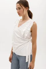 Musculosa blanca cruzada con escote en V que se ata alrededor del cuerpo. Confeccionada en algodón suave. El detalle de volados en 3D recorre el frente y los hombros.
