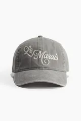 Gorra de algodón color gris con visera curva y bordado frontal con la inscripción "Le Marais" en color blanco.