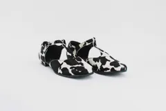 Zapato flat de cuero con estampado de vaca en blanco y negro, con tira delantera y hebilla lateral.