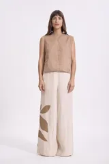 Pantalón ancho de lino color beige claro con estampado grande de hojas en color marrón en la parte inferior de la pierna izquierda. El pantalón tiene un corte holgado y tiro alto.