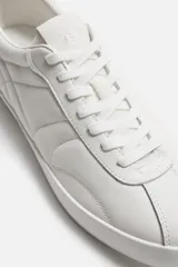 Zapatillas de cuero blanco con cordones y suela plana.