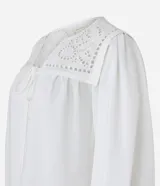 Blusa blanca amplia de viscosa, con lazo delantero, mangas largas abullonadas y canesú con encaje richelieu.