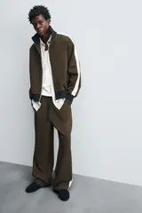 Pantalón jogger color verde oliva, corte relaxed fit, con cintura elástica ajustable con cordón, bolsillos laterales y detalle de bolsillo de vivo en la espalda. Presenta una banda lateral color crema a contraste.