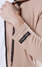 Campera beige con cierre frontal, capucha con cordón ajustable, bolsillos laterales con cierre y calce regular.