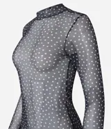 Blusa de tule transparente color negro con lunares blancos, cuello alto y mangas largas.