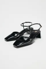 Zapato destalonado acharolado negro, con punta cuadrada, tacón ancho y pulsera al tobillo con hebilla.
