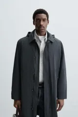 Parka larga color verde oscuro, con capucha desmontable, cuello solapa, bolsillos laterales y cierre frontal con cremallera oculta y botones a presión. Incluye chaleco interior acolchado desmontable.
