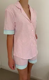 Conjunto de pijama de algodón a rayas verticales rosas y blancas, con detalles en celeste. Incluye camisa de manga corta con botones y bolsillo en el pecho, y shorts con cintura elástica.
