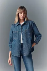 Camisa de denim azul con apliques metálicos plateados, de calce amplio, cuello camisero, cierre frontal con botones a presión, mangas largas con puños abotonados y dos bolsillos con solapa abotonada en el pecho.