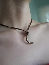 Gargantilla marrón de cuero con dije de bronce en forma de letra M.