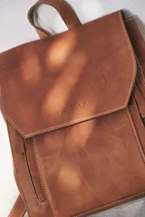Mochila de cuero color marrón con cierre de solapa y hebilla, tamaño mediano.