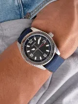 Reloj Guess con caja plateada, esfera negra con números arábigos y correa de tela azul.