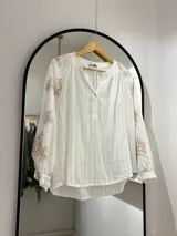 Blusa blanca con escote en pico y botones en el frente. Detalles florales bordados en mangas.