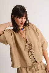 Blusa color crema confeccionada en lino, con mangas cortas, escote en V y lazos frontales.