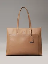 Cartera tote Calvin Klein color tostado, de tamaño mediano, confeccionada en cuero sintético granulado con textura de logo monograma en el bolsillo delantero. Tiene asas fijas, cierre magnético, bolsillo exterior, compartimento interior con cremallera y colgante extraíble con logo.