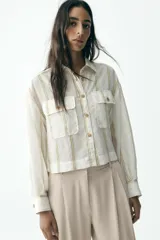 Camisa blanca a rayas verticales color beige, de corte recto, con cuello solapa, manga larga y dos bolsillos de parche en el pecho.