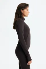 Campera deportiva corta color marrón, de corte ajustado, con cuello alto, cierre frontal con protección para el mentón y mangas largas con abertura para el pulgar. Confeccionada en tejido funcional SoftMove™ y DryMove™.
