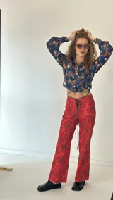 Camisa crop azul con estampado floral multicolor, cuello camisero, mangas largas con puños abotonados y lazos para atar en la cintura.