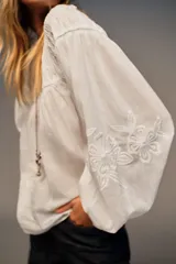 Camisa blanca de cuello redondo con detalle de nido de abeja y entredoses. Manga larga con bordados a tono y cierre trasero con botones.