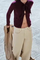 Chaqueta color borgoña de tejido de punto con lana y alpaca. Tiene cuello redondo con lazo de satén, manga larga y cierre frontal con botones. Presenta dos bolsillos de parche en el frente.