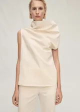 Blusa color crema sin mangas, con cuello asimétrico drapeado y corte recto.