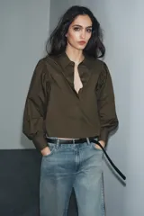 Camisa blanca de popelina con cuello solapa, manga larga abullonada con puño y bajo recto. Cierre frontal con botones ocultos por solapa.