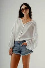 Blusa blanca de manga larga con volados en los puños y escote en V con botones frontales.