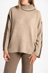 Sweater de punto color beige jaspeado, con cuello alto acanalado y franjas verticales de tejido marrón brillante en las mangas. Presenta un calce holgado (oversize).