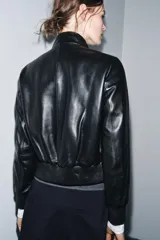 Chaqueta bomber de cuero negra con cuello alto, cierre frontal con cremallera, bolsillos laterales y puños y bajo elásticos.