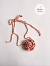 Gargantilla tejida a mano en algodón color rosa, con forma de rosa y tiras para atar.
