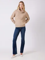 Buzo de punto grueso color beige, con cuello volcado y textura en relieve. Tiene mangas largas de corte hombro caído y puños anchos.