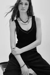 Musculosa negra de tejido de punto, ajustada al cuerpo, con escote en V y detalles de pequeños apliques blancos (similares a tachas o puntos) bordeando el escote y la cintura.