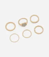Set de seis anillos dorados con diferentes diseños: uno liso, uno con textura, uno con una flor gris, uno con strass y uno con forma ondulada.