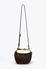 Bolso mini trenzado color marrón con asa de mano dorada metálica y doble asa bandolera ajustable y extraíble. Tiene forro, bolsillo interior y cierre mediante cremallera.